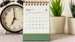 Desk calendar that reads June 2024 sits centered on desk with plants and a retro bell alarm clock blurred in background