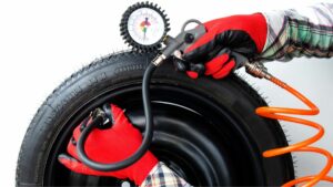 Close up of a mechanic inflating a car tire and checking pressure with pressure gauge against a white background