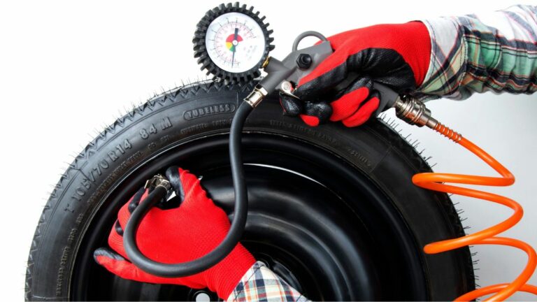 Close up of a mechanic inflating a car tire and checking pressure with pressure gauge against a white background