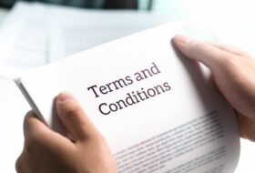 Close up of white hands holding papers that read 'terms and conditions' in front of a blurred office background