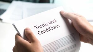 Close up of white hands holding papers that read 'terms and conditions' in front of a blurred office background