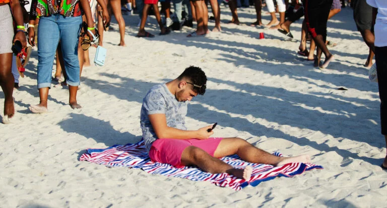 A Man Uses His Phone on the Beach, Perhaps Like Florida Online Sports Betting Participants