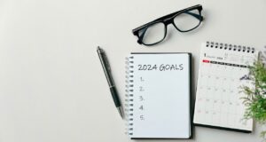2024 goals Text on Note Pad with calendar, glasses on the table.