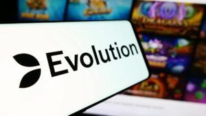 black on white Evolution Gaming logo phone on smartphone screen. Blurred mobile casino lobby in backgrouund