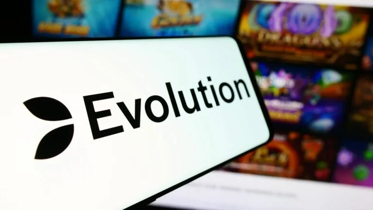 black on white Evolution Gaming logo phone on smartphone screen. Blurred mobile casino lobby in backgrouund