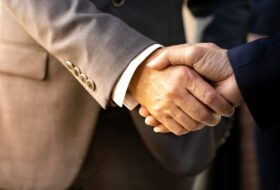 Close up of business handshake. Male coded arms wearing one gray and one navy business suit each shake hands