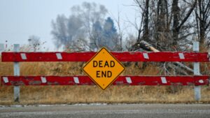 close up of a red fence at end of grey and gloomy rural road featuring a dead end street sign