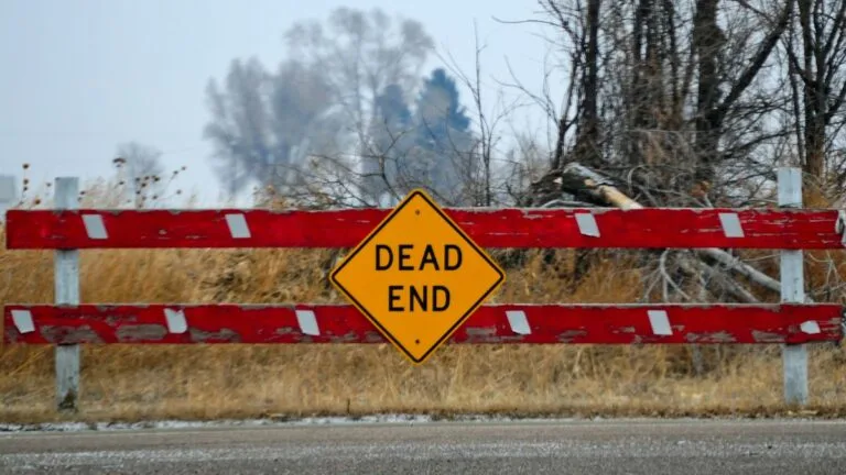 close up of a red fence at end of grey and gloomy rural road featuring a dead end street sign