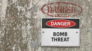 rough concrete wall dispaying white sigh with black and red lettering that reads danger in red and white, with bomb threat written under it in black a faded red painted oval on concrete above encircles equally faded red danger