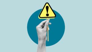 Illustration features grayscale hand holding yellow and black exclamationpoint alert sign on pale blue background with darker blue circle behind hand