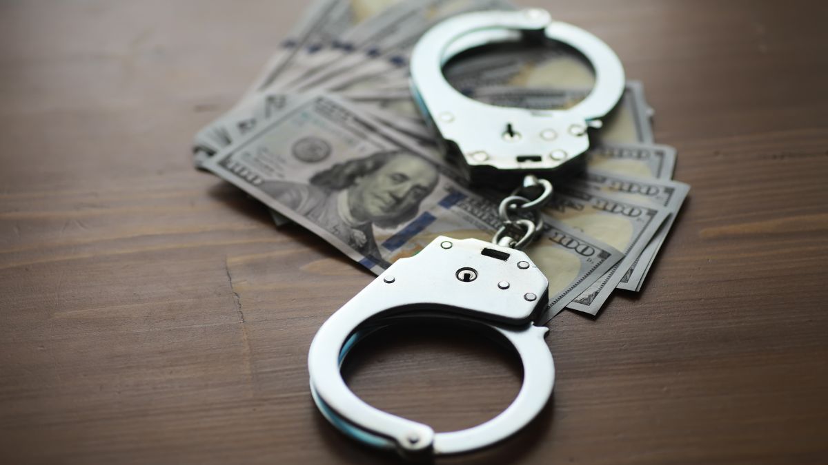 a pair of handcuffs over a series of hundred dollar bills