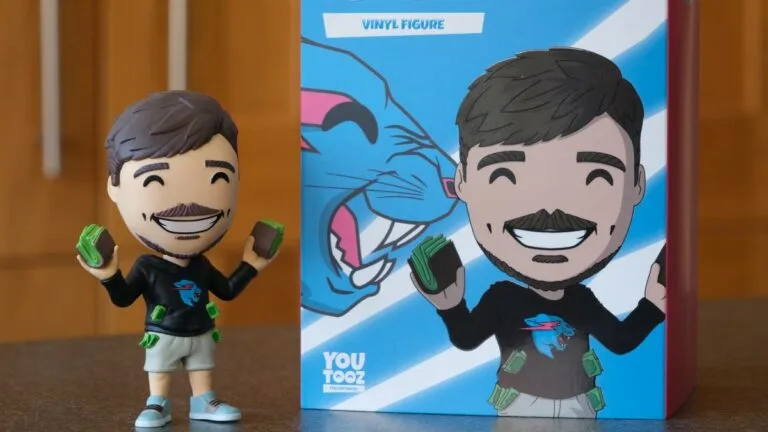 MrBeast You Toox vinyl figure golding fast stacks of cash sits on table next to retail box with figure's image. Wood paneled walls fill background