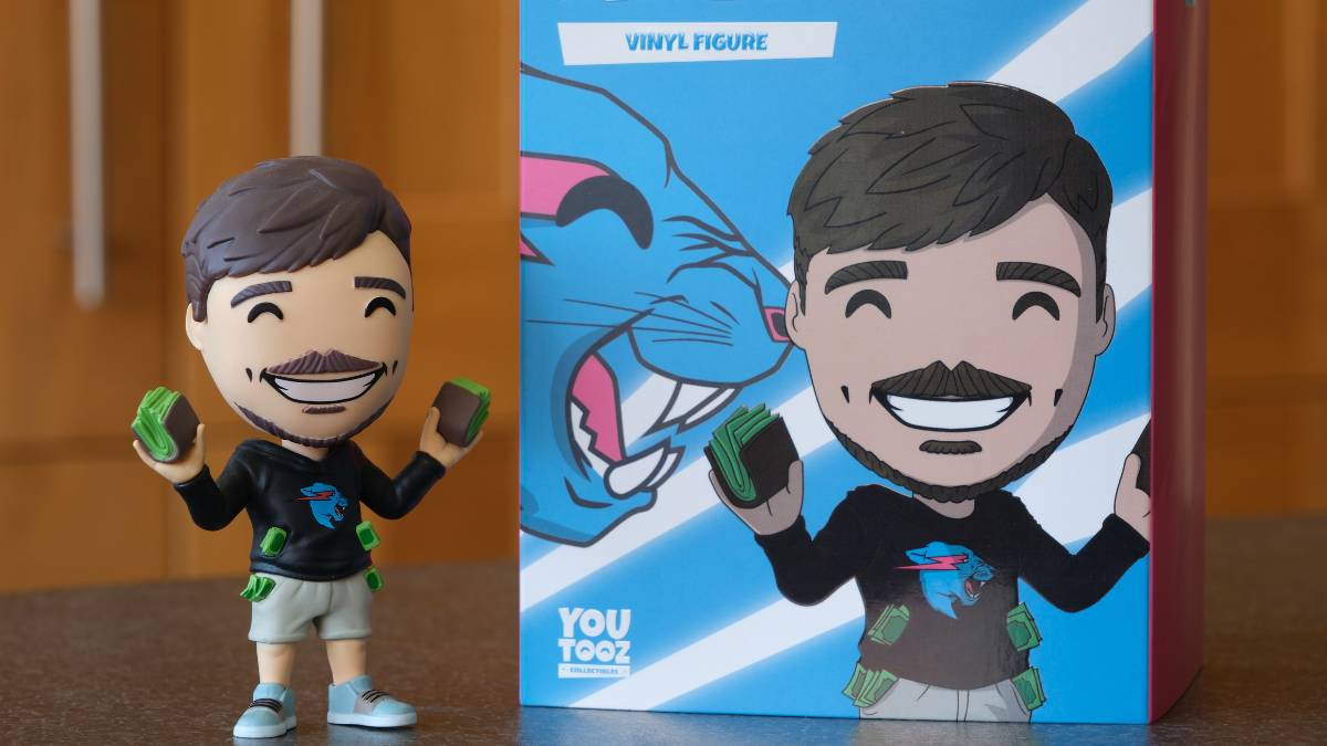 MrBeast You Toox vinyl figure golding fast stacks of cash sits on table next to retail box with figure's image. Wood paneled walls fill background