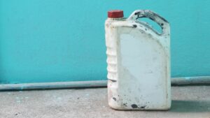 Old empty white gallon gas can with red cap sits in front of a turquoise blue wall