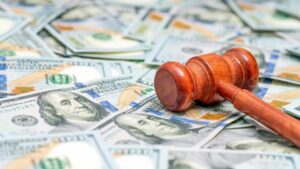 Cherry-wood judge's gavel lays diagonally across pile of US dollar bills scattered across table top