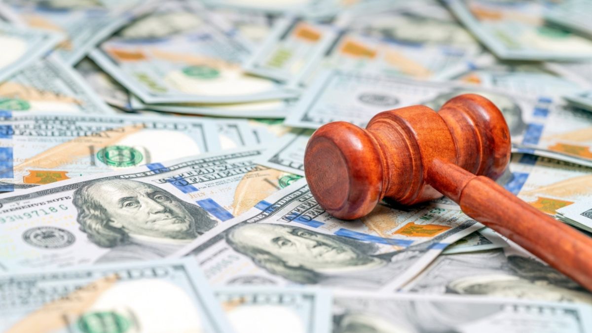 Cherry-wood judge's gavel lays diagonally across pile of US dollar bills scattered across table top