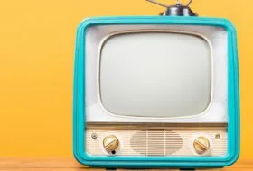 Retro TV with Antenna and turquoise frame sits on desk/flat surface in front of bright yellow wall