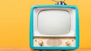 Retro TV with Antenna and turquoise frame sits on desk/flat surface in front of bright yellow wall