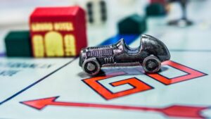 Color close up of monopoly voard. Silver car game piece sits on 'GO' corner of board