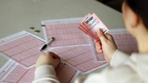 a person filling out a lottery ticket form while holding a trio of lottery tickets
