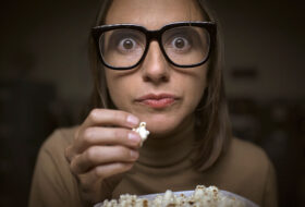 Woman glued to television eating popcorn
