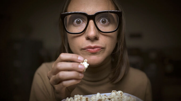 Woman glued to television eating popcorn
