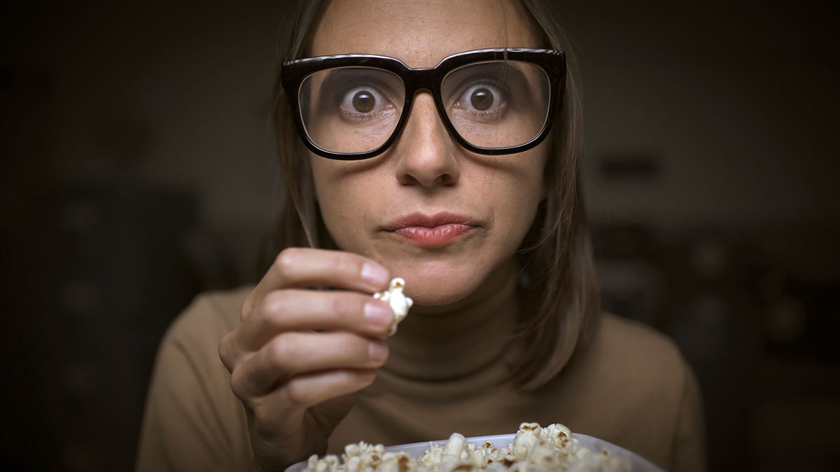 Woman glued to television eating popcorn