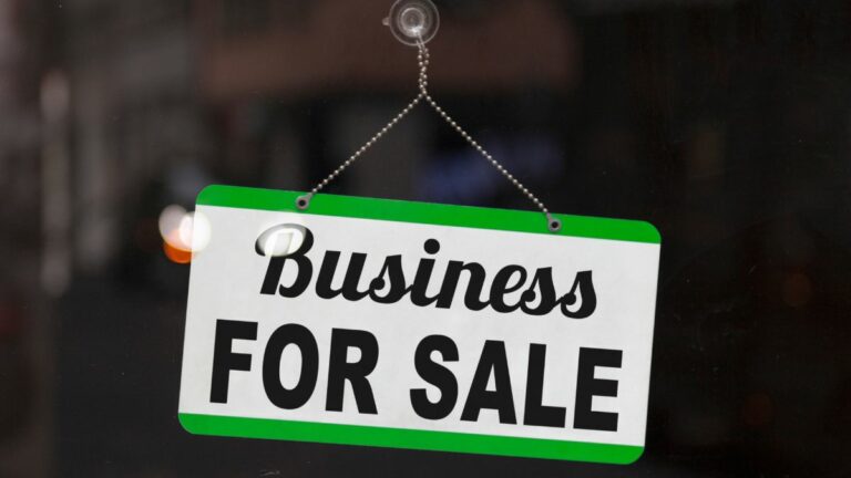 Black and white sign hanging from suction cup on glass door. Top and bottom margins of sign are green. Sign reads business for sale