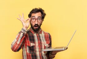a man looking silly with his glasses while looking at his laptop computer