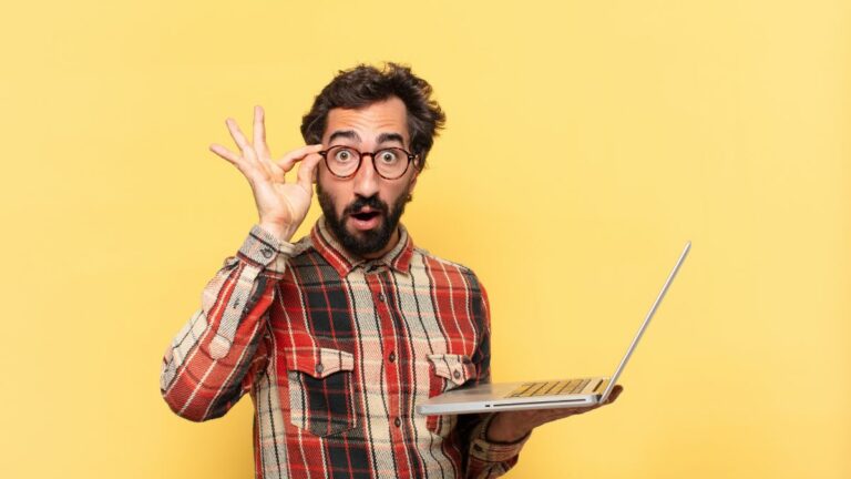 a man looking silly with his glasses while looking at his laptop computer
