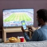 man betting on a sports betting app while watching football match
