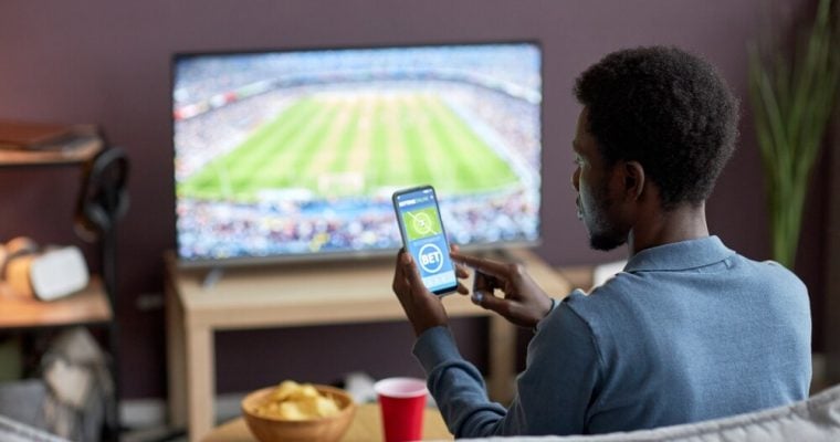 man betting on a sports betting app while watching football match