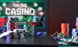 Concept of playing online casino games with laptop with gaming application on plush green mat and stacks of chips on top and around. Front view.