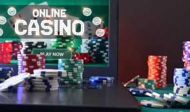 Concept of playing online casino games with laptop with gaming application on plush green mat and stacks of chips on top and around. Front view.
