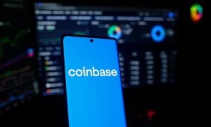 Coinbase logo on a smartphone in front of a trading screen setup