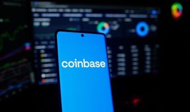 Coinbase logo on a smartphone in front of a trading screen setup