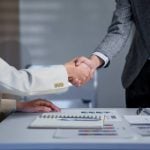 Two business professionals engage in a handshake across a desk