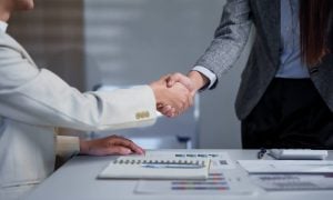 Two business professionals engage in a handshake across a desk