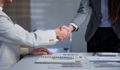 Two business professionals engage in a handshake across a desk