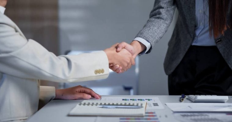 Two business professionals engage in a handshake across a desk