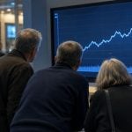 A group of people observe a large screen displaying a rising stock chart and financial data bars.