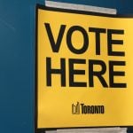 vote here capital letters in black on yellow background with toronto logo masking taped to blue door
