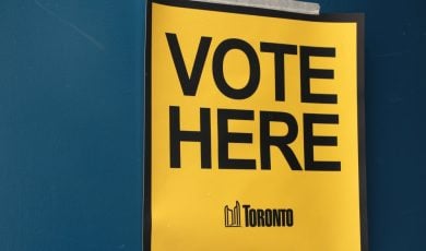 vote here capital letters in black on yellow background with toronto logo masking taped to blue door