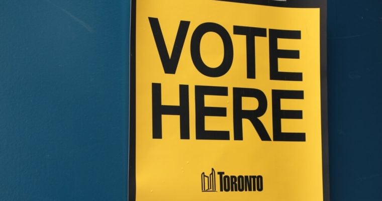 vote here capital letters in black on yellow background with toronto logo masking taped to blue door